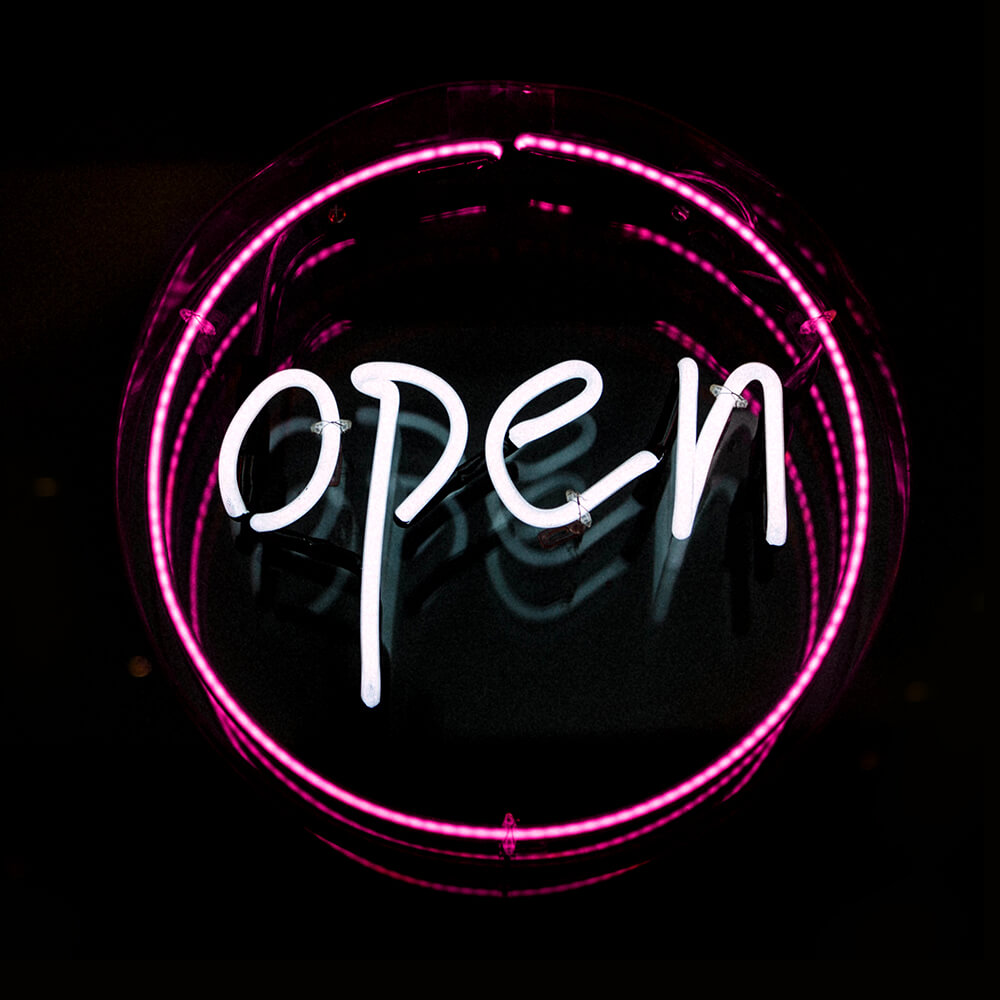 A neon light sign that reads "open" in white neon light. It is surrounded by a circle of pink neon light.