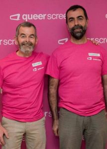 Two Queer Screen volunteers in pink t-shirts stand side by side smiling