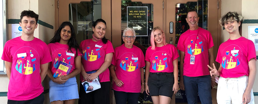 10 volunteers of various ages wearing their Queer Screen Volunteers t-shirts stand outside a cinema
