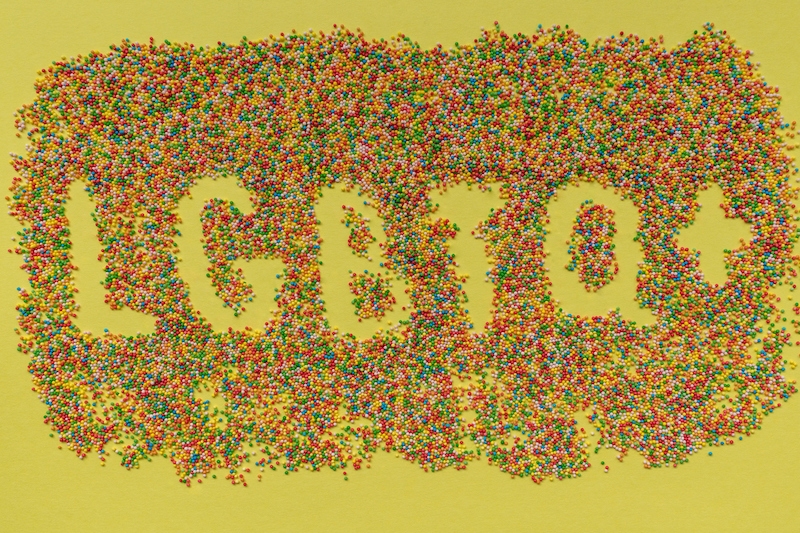 LGBTQ word and plus sign mwritten in sprinkles on a yellow background.