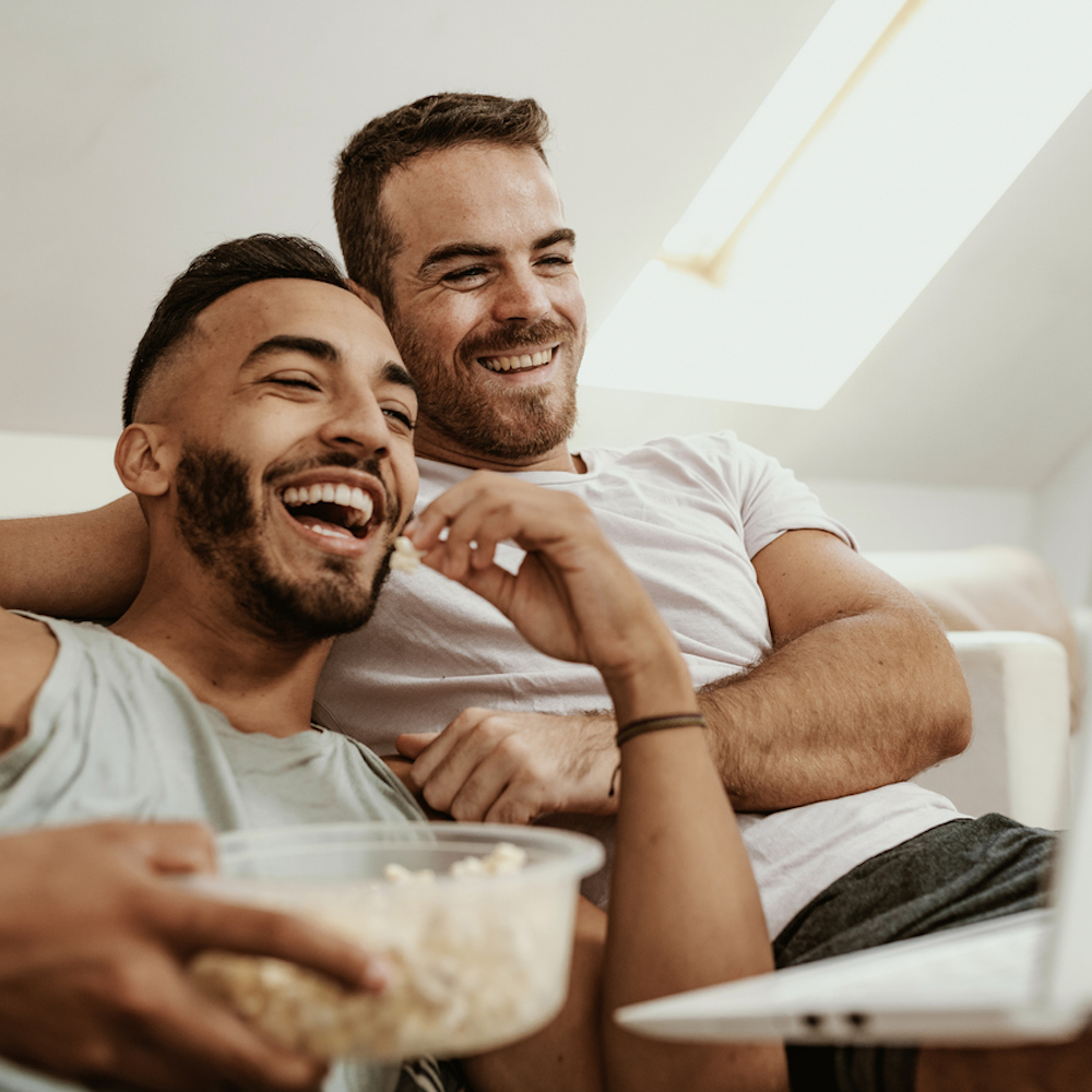 Two men watching a laptop, eating popcorn