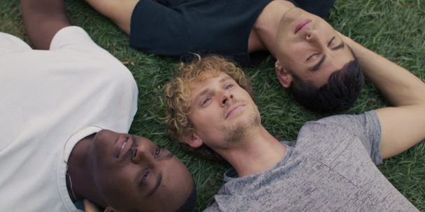 Three people laying on the grass. Their heads close together.