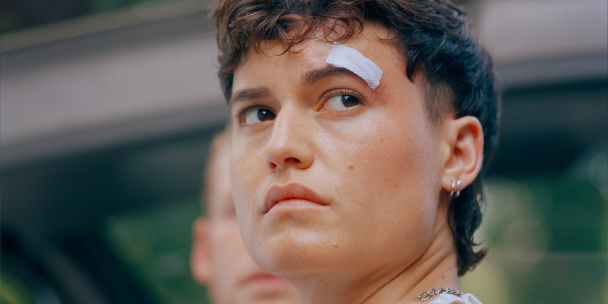 A close up of a person turning back to look at something. They have a bandaid across their eyebrow.