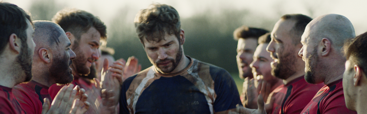 Rugby player Mark, walks past other rugby players as they clap.