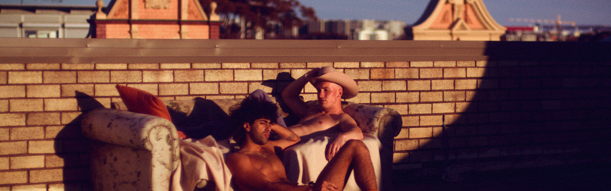 Casey and Tib sit shirtless on a couch in the film Lonesome.