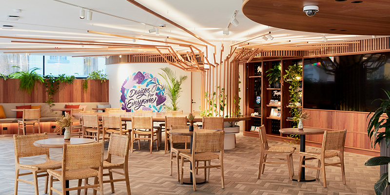 Photograph of the interior entertaining space at Canva Space containing a large amount of tables and chairs and wood paneling, and lush greenery.