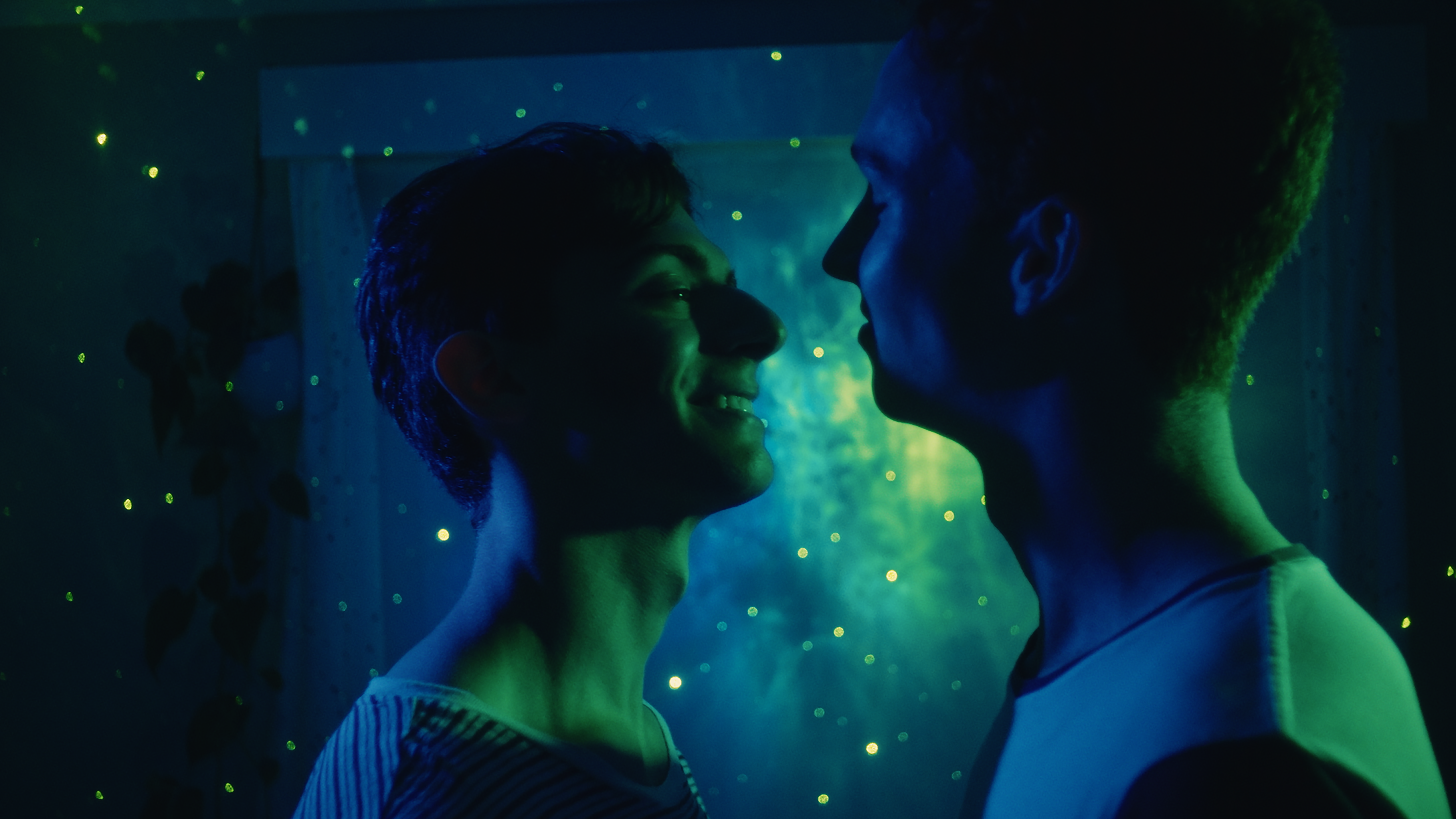 Two men smile as they look into each other's eyes, bathed in green light