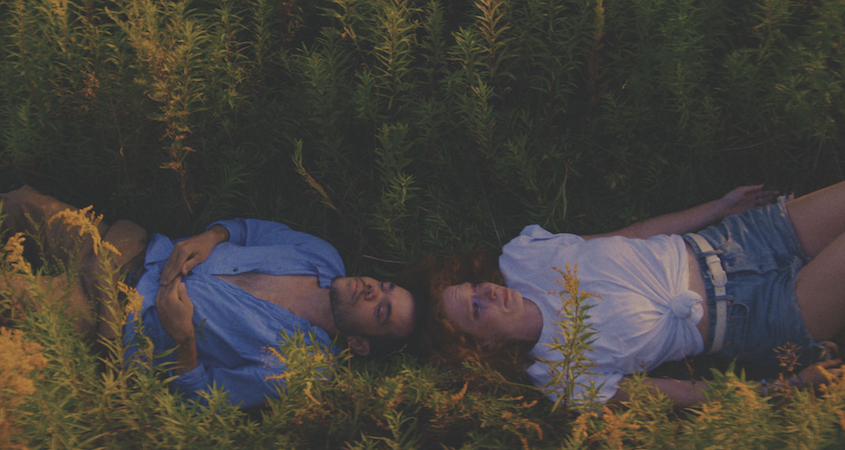 Two people lie head to head in a field.