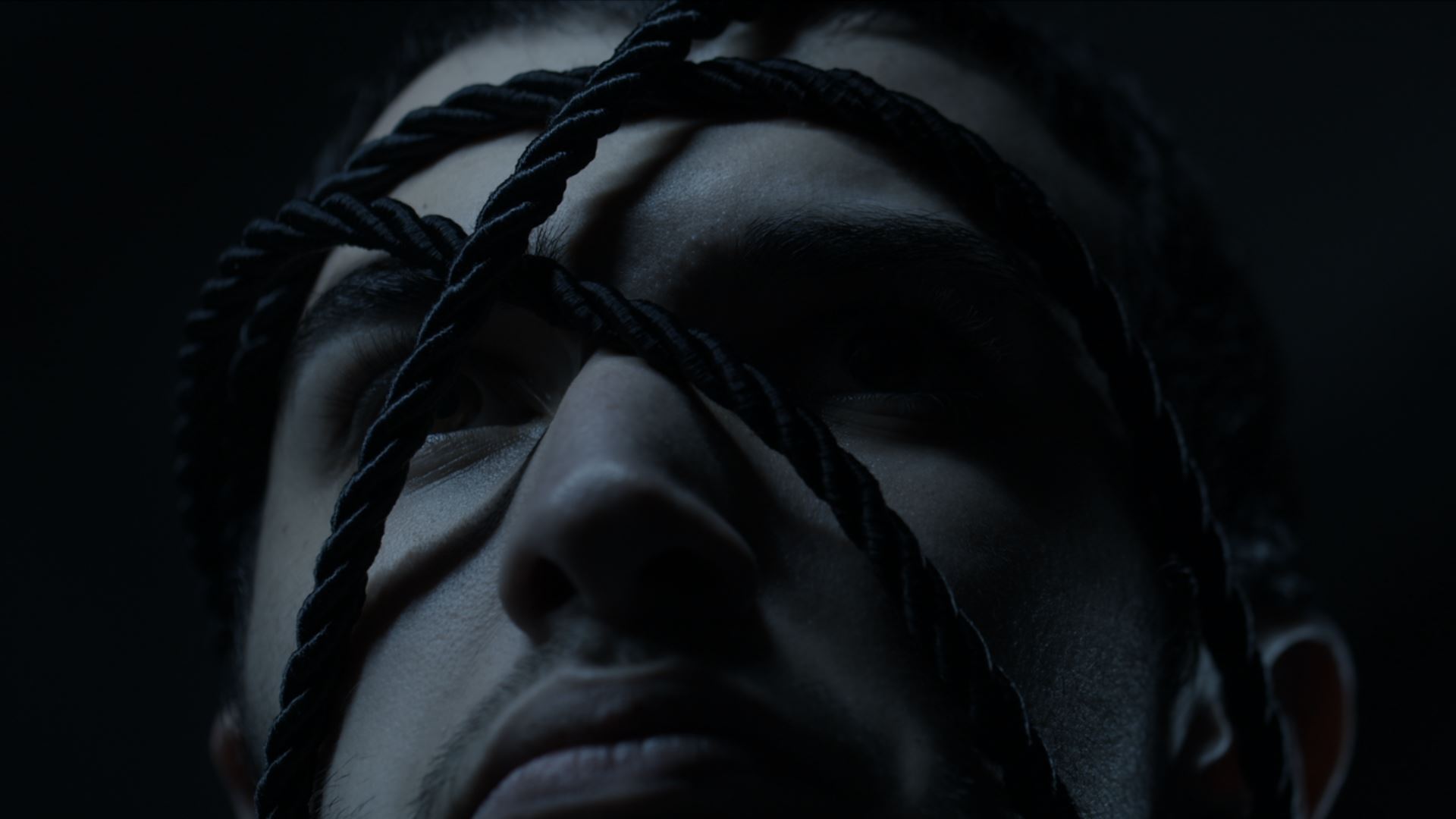 A dark image of a person's face, covered in black rope.