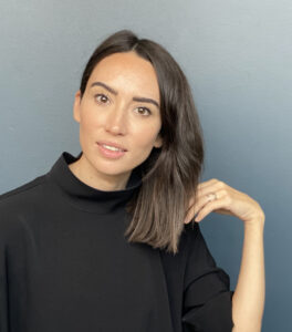 Portrait of Andria Wilson Mirza wearing a black outfit with her hand on her shoulder.