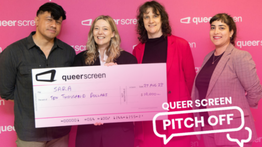 Four people against a pink wall with a giant cheque