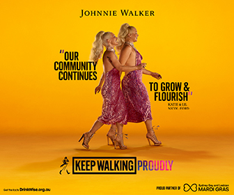 Johnnie Walker advertising. Text reads: Our community continues to grow and flourish. Keep Walking Proudly. Image of two people with their hair done up high, and wearing burgundy evening dresses and heads walking from the left side of the banner to the right side of the banner in a gold room.