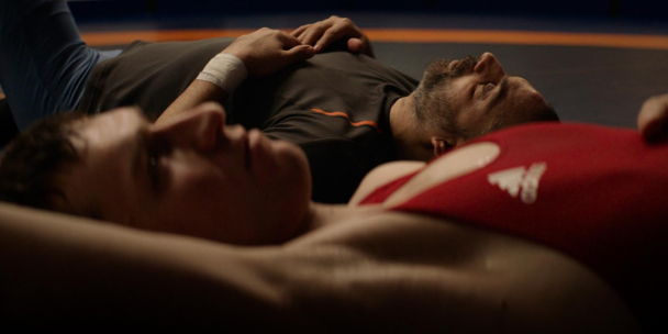 'Opponent'. Two people laying on what appears to be a wrestling mat. Both on their backs, looking up to the ceiling.