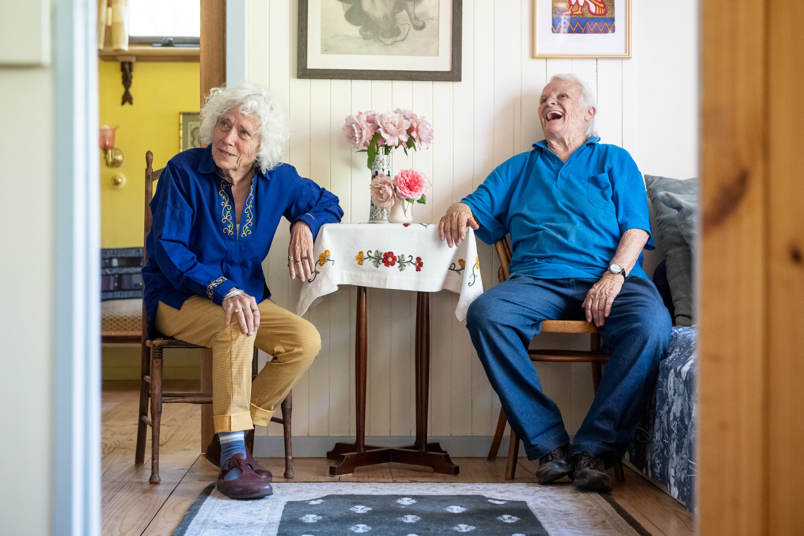 Two older people sit at a table together, smiling.