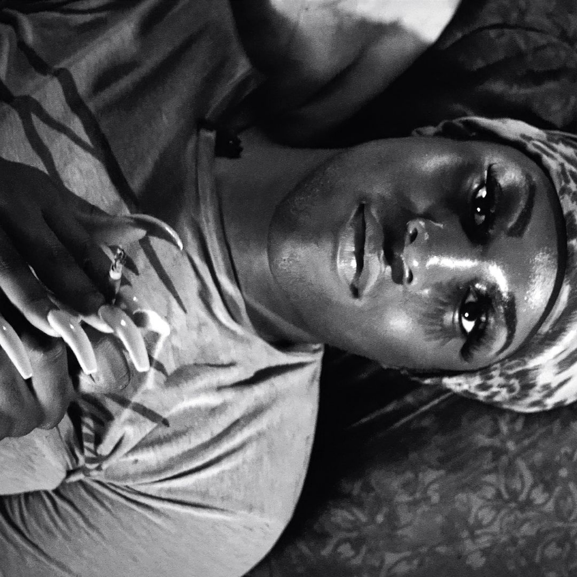 A woman lies on her back staring up into the camera, in black and white.