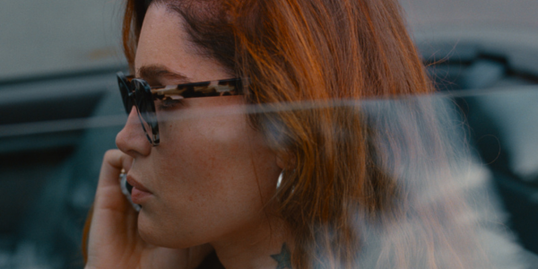 A still from the film 'Monica'. A close-up of a person wearing sunglasses. They are on the phone.