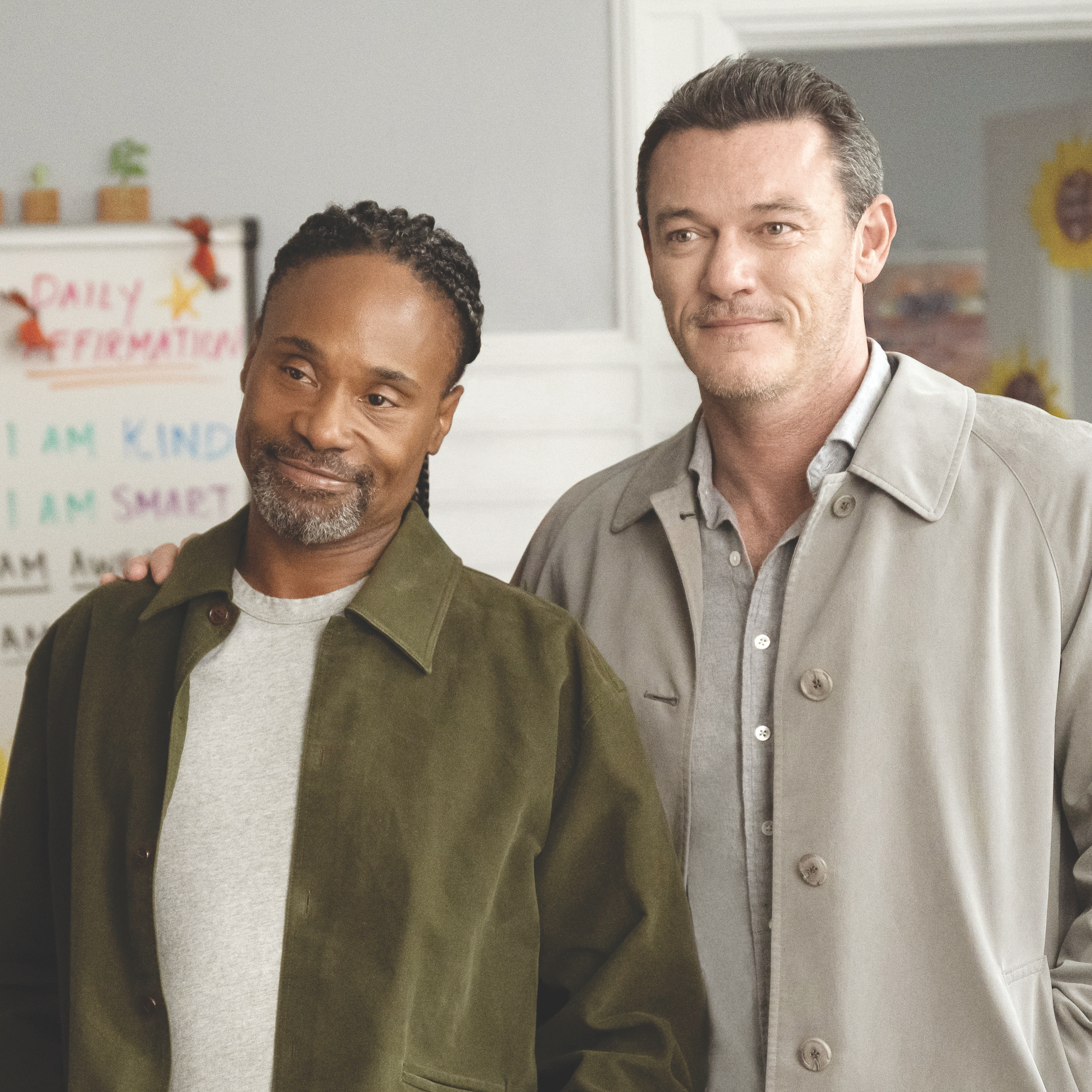 Two men, Billy Porter and Luke Evans, stand side by side with an arm wrapped around the other.