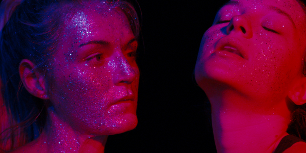A still from the film 'Silver Haze'. Two people, seemingly dancing. The lighting is a deep pink and they are covered in glitter.