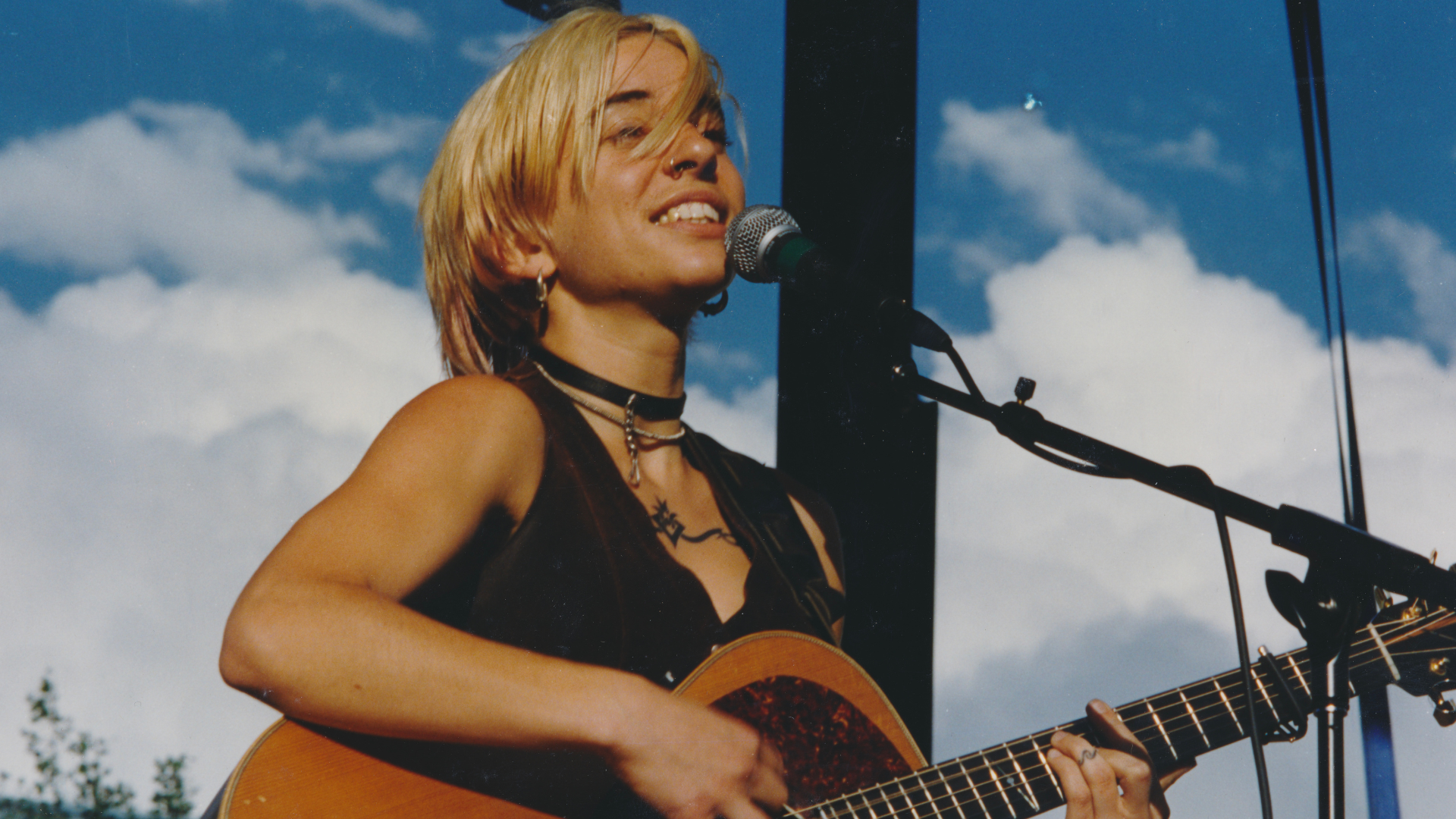 A young Ani Di Franco stands at a microphone, singing and playing her guitar