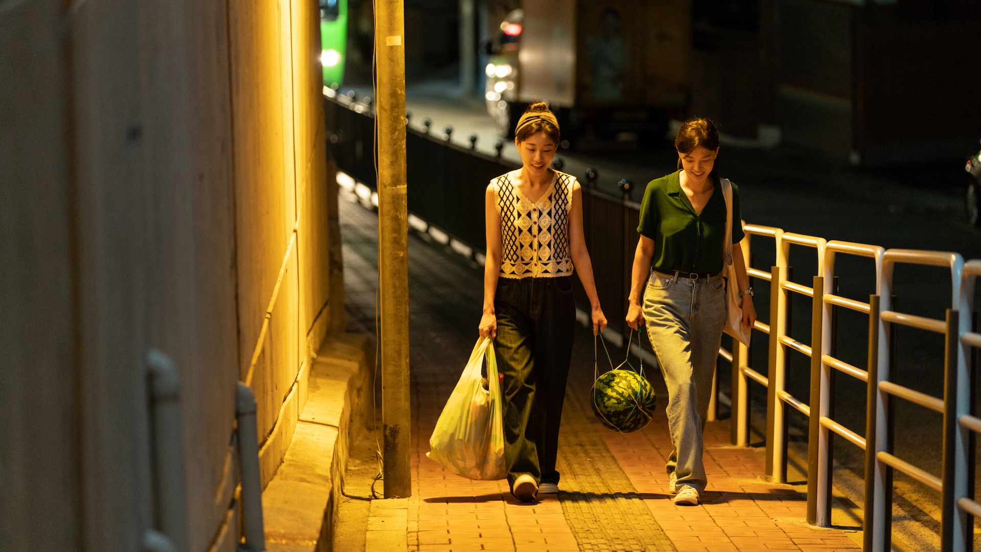 Two. young women walk down a footpath together, carrying groceries