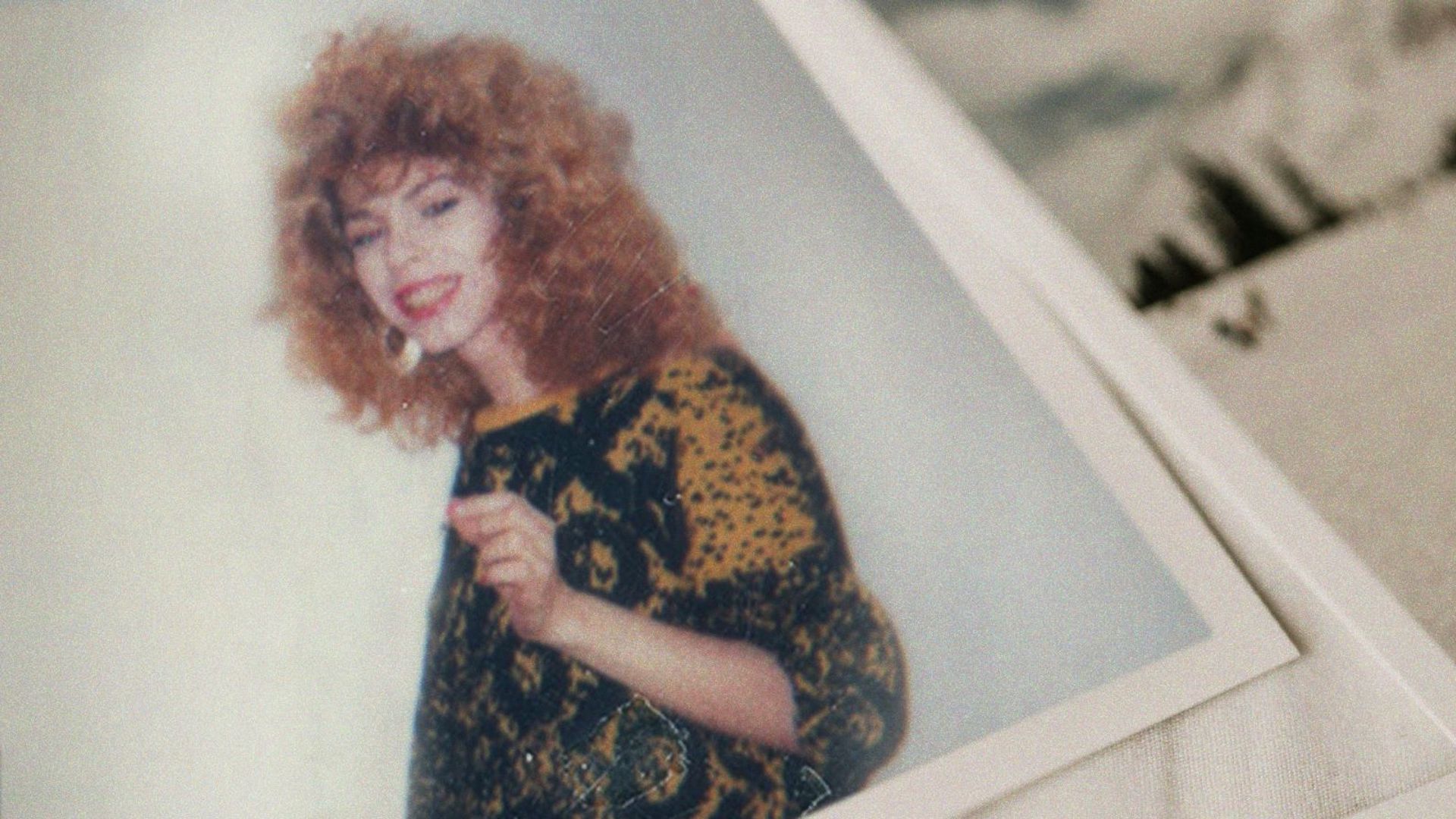 An aged printed film photograph of a woman with distinctly 1980s clothes and hairstyle