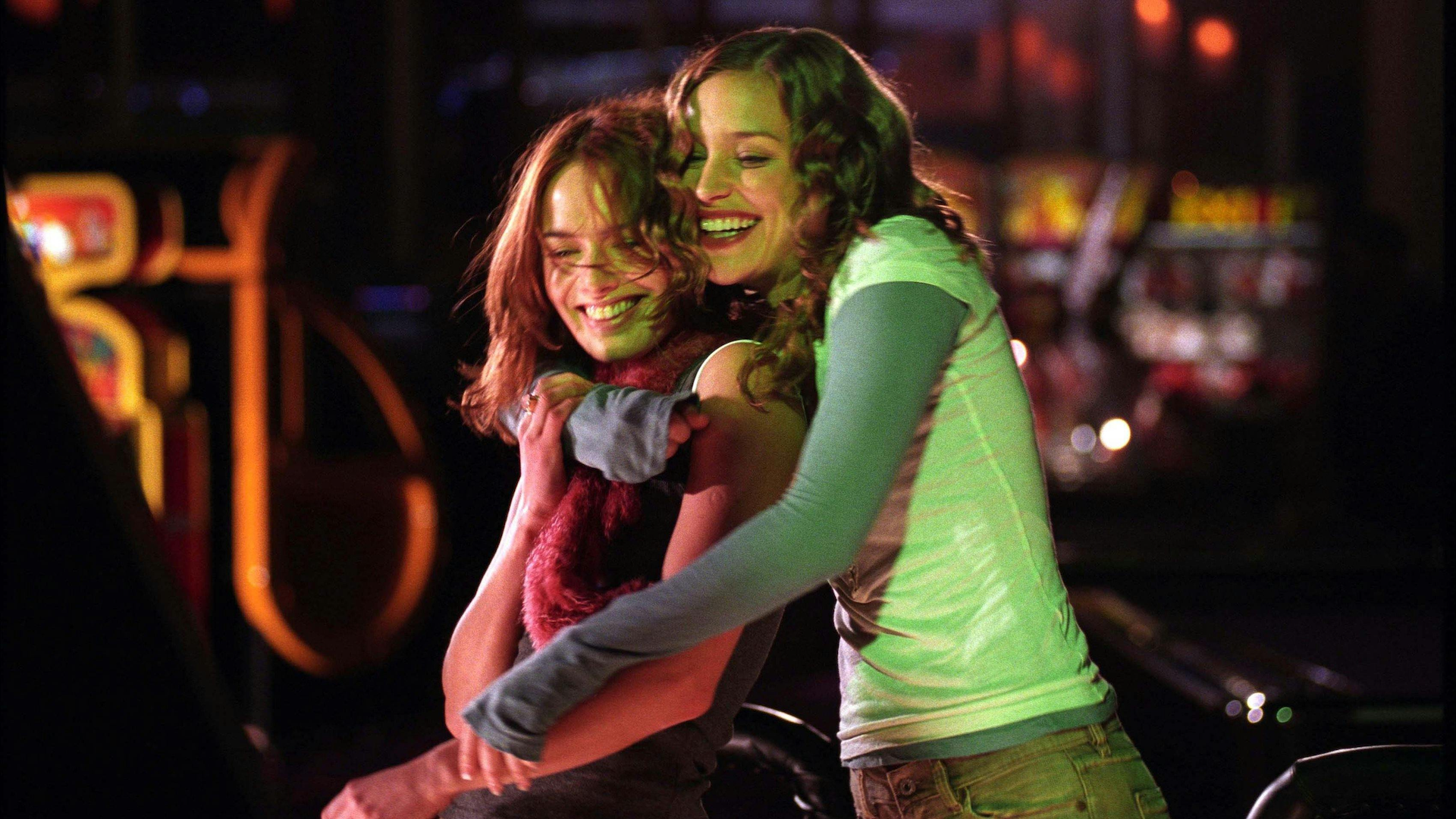 A woman hugs another woman from behind, as they both smile