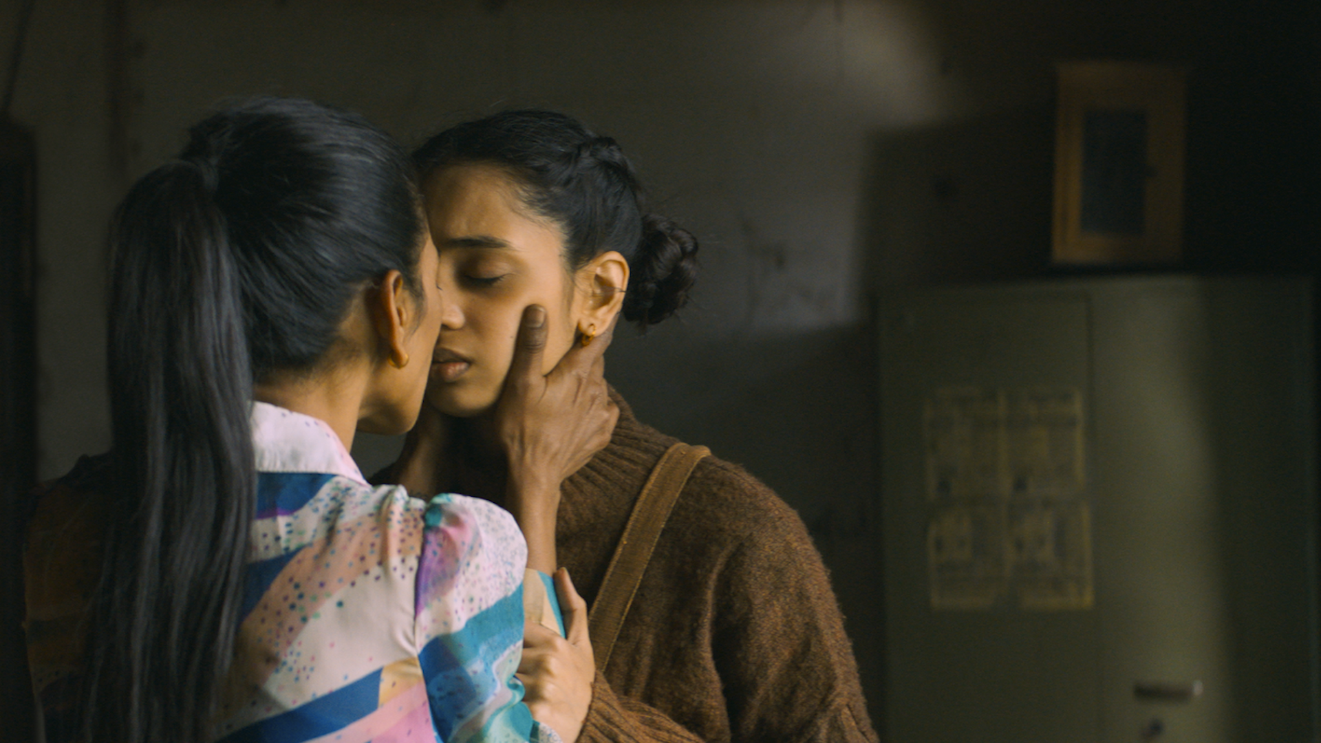 Two women look into each other's eyes as they hold onto each other, one grasping the other's face in her hands while the other grips her arms