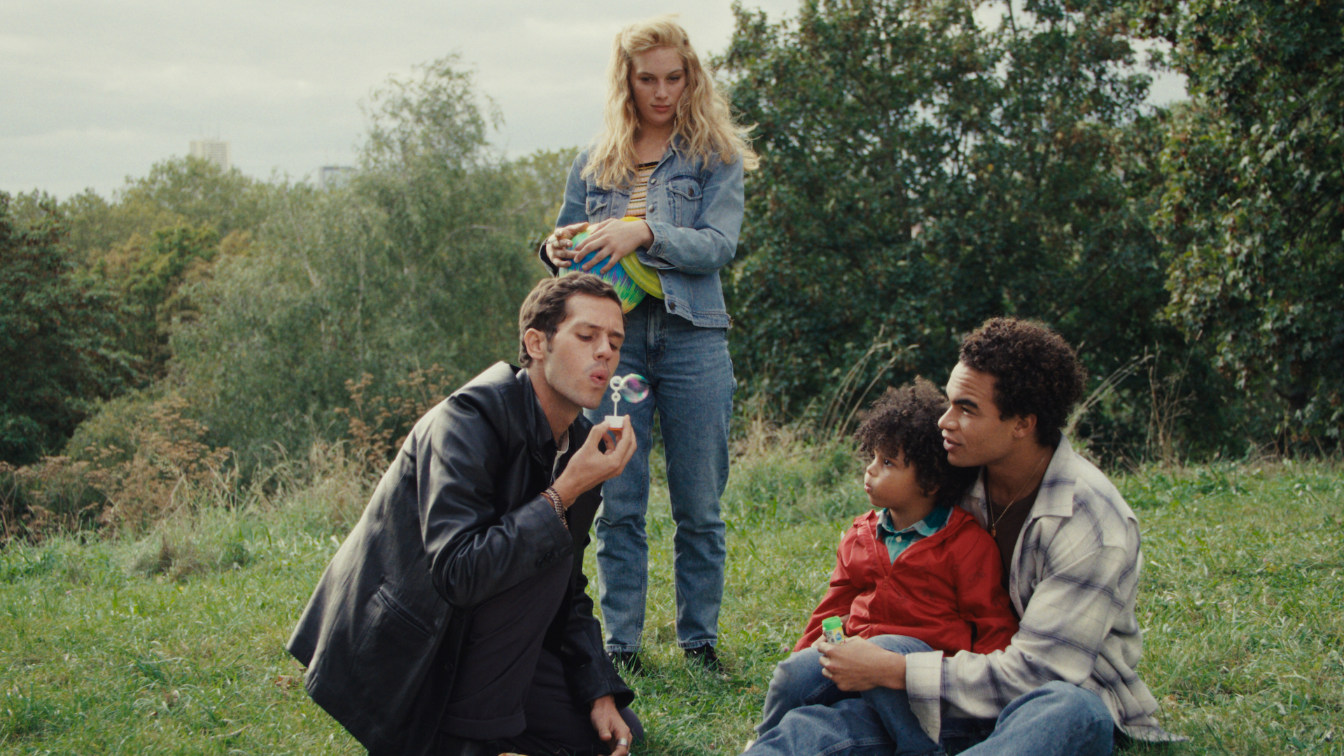 A man blows bubbles for a child being held by another man, while a woman stands behind them looking on