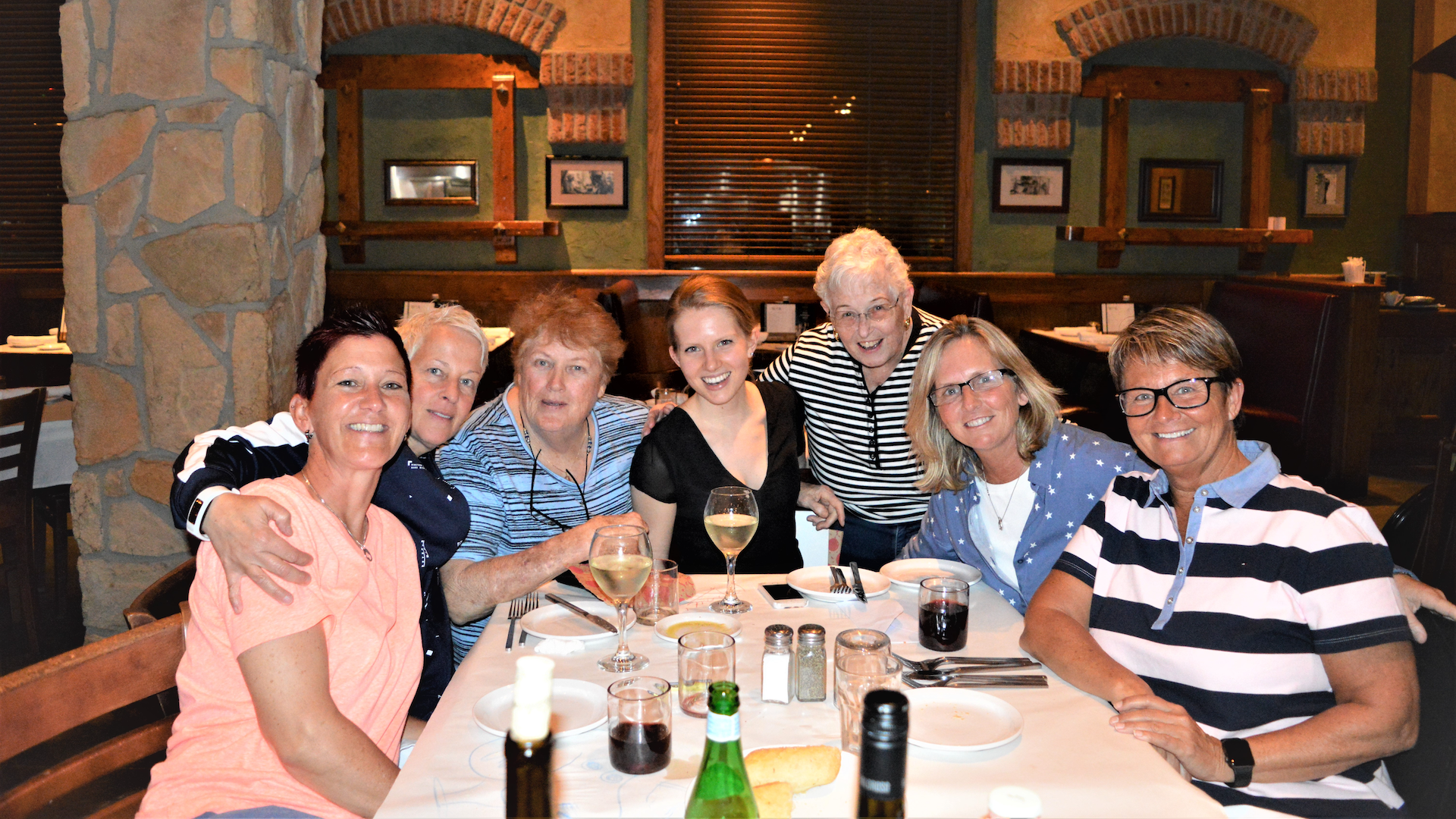 Seven women representing three generations of a family pose for a photo around a table in a restaurant