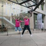 Two people in pink tshirts jumping in the air.