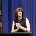 A woman in black clothing behind a lectern.